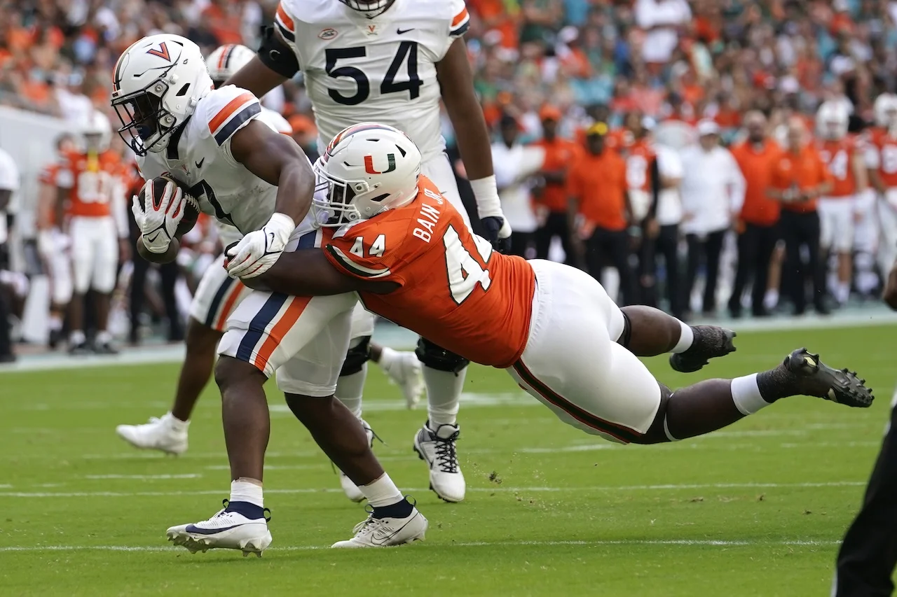 Virginia running back Mike Hollins, left, runs before being tackled by Miami defensive lineman Rueben Bain Jr. (44) during the first half of an NCAA college football game, Saturday, Oct. 28, 2023, in Miami Gardens, Fla. (AP Photo/Lynne Sladky)
